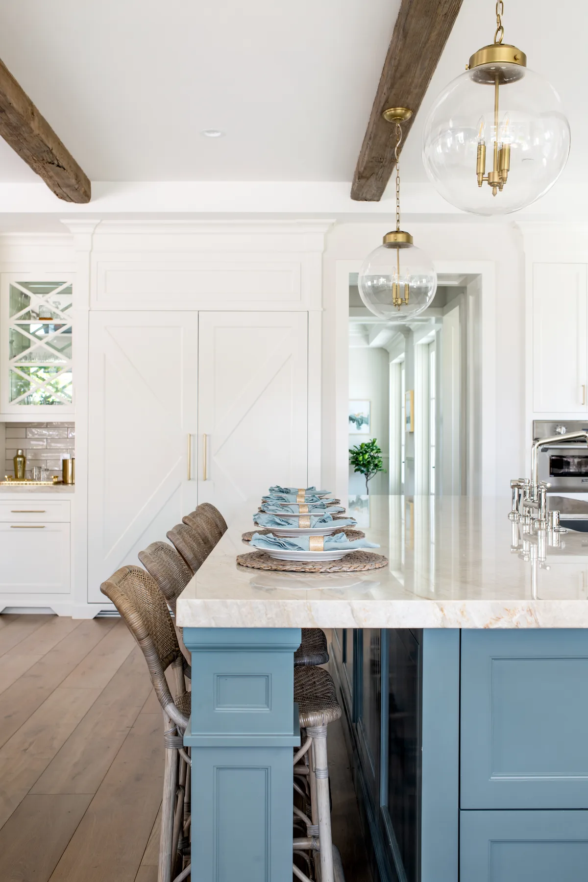 White shaker cabinetry, a blue island and reclaimed wood ceiling beams under glass globe pendants warm this South Bay farmhouse kitchen.