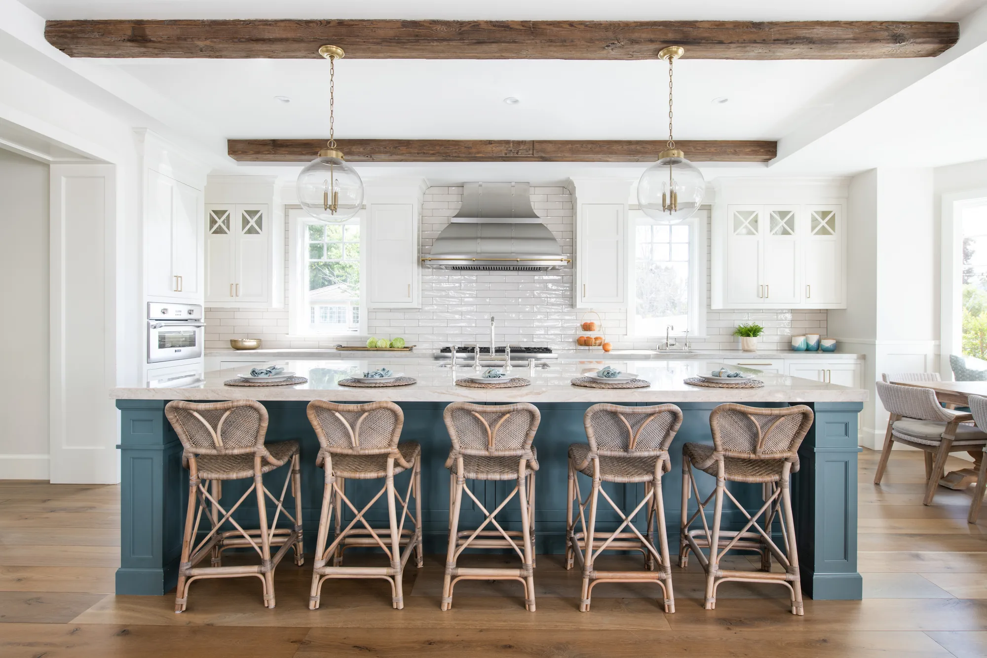 Reclaimed wood ceiling beams and a blue waterfall island with brass globe pendants bring farmhouse warmth to white shaker cabinetry.