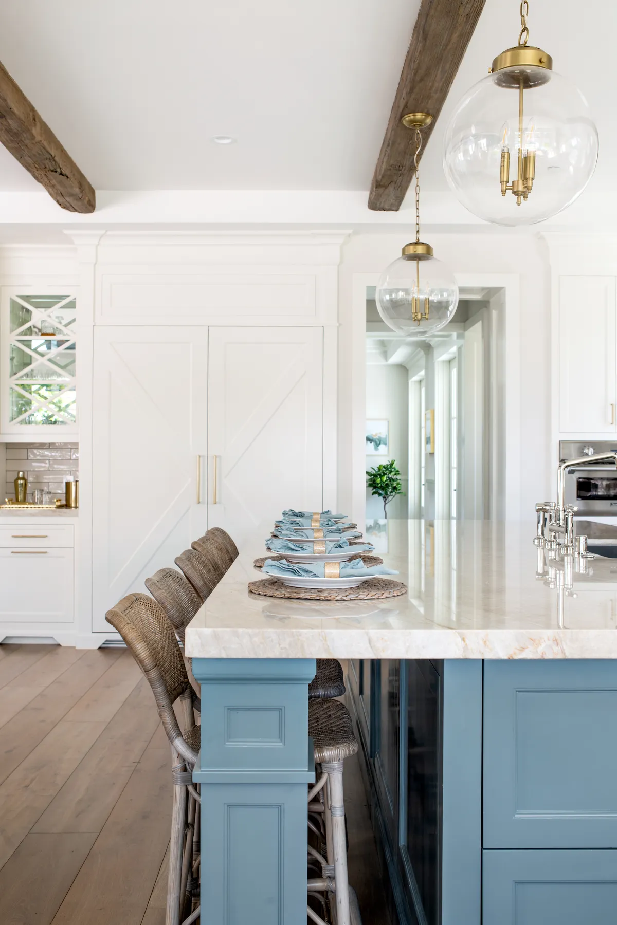 Deep-blue island with woven counter stools, brass hardware and white shaker cabinetry in a tall Palos Verdes coastal kitchen.
