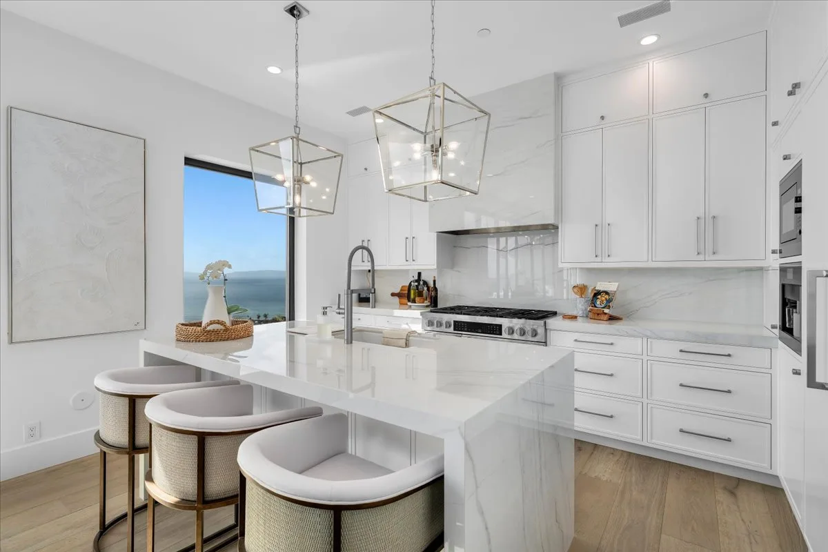 White marble kitchen with a waterfall island and lantern pendants beside an ocean-view window on the Palos Verdes Peninsula.