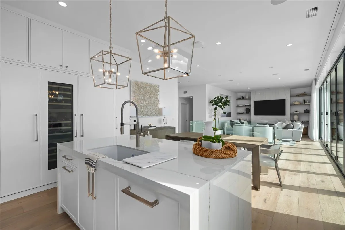 Marble island with a prep sink anchoring an open-plan white kitchen that flows to indoor-outdoor living in a Torrance ranch remodel.