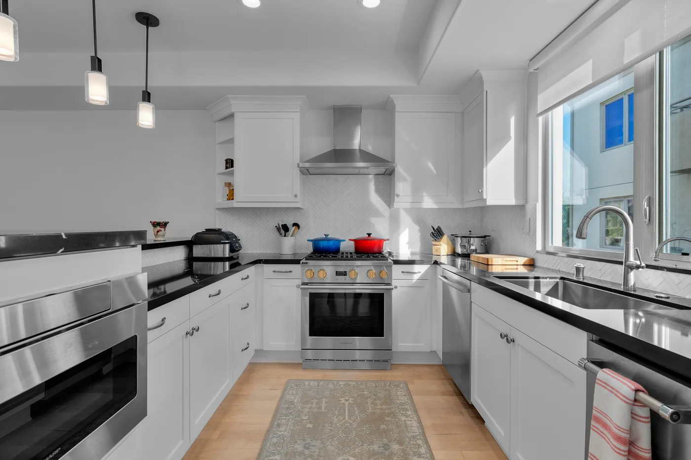 Black countertops and a marble herringbone backsplash behind a stainless Wolf range in a bright Palos Verdes kitchen.